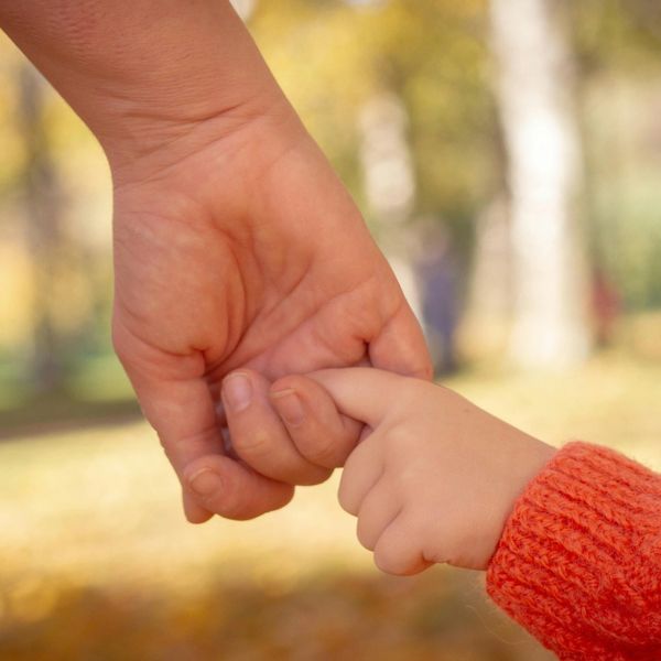 Adult and child holding hands gently outdoors in autumn.