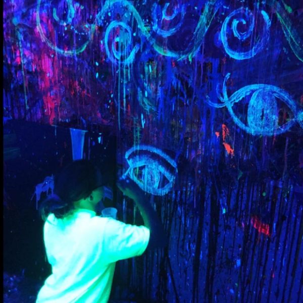Person painting glowing eyes and swirls under blacklight.