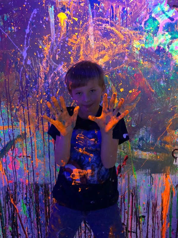 Child with neon paint on hands in front of a colorful wall.