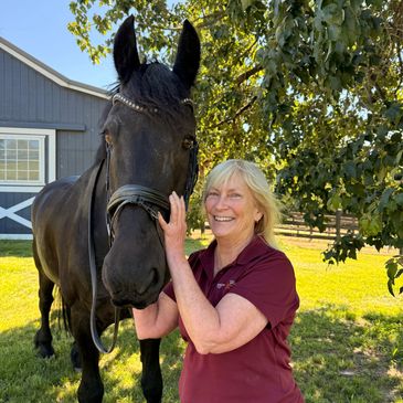 Woman smiling while holding a black horse's face.