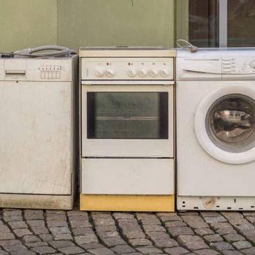 Old kitchen appliances arranged outdoors on cobblestone ground.