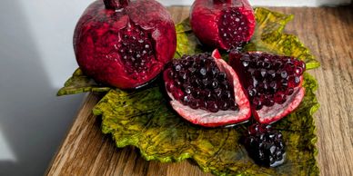 Realistic pomegranate sculptures on a green leaf plate on a wooden surface.