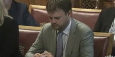 A man in a suit sitting and focusing on his hands in a formal setting.