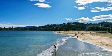 Sunny beach day with people enjoying the water and sand under a bright blue sky.