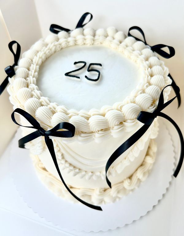 Elegant white cake with black ribbons and the number 25 on top.