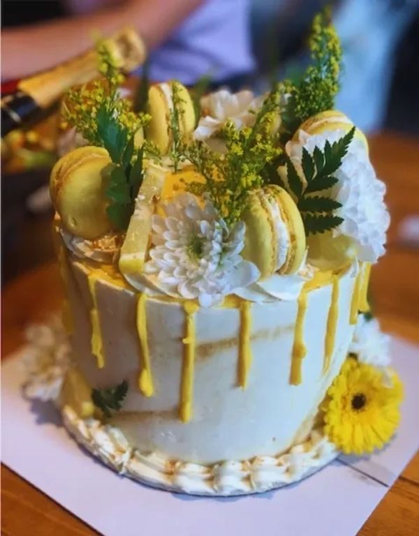 Elegant white and yellow drip cake with macarons and flowers.