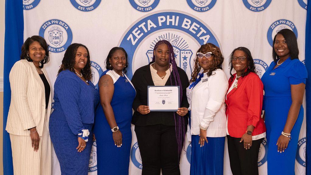Group of women posing in front of Zeta Phi Beta banner, one holding a certificate.
