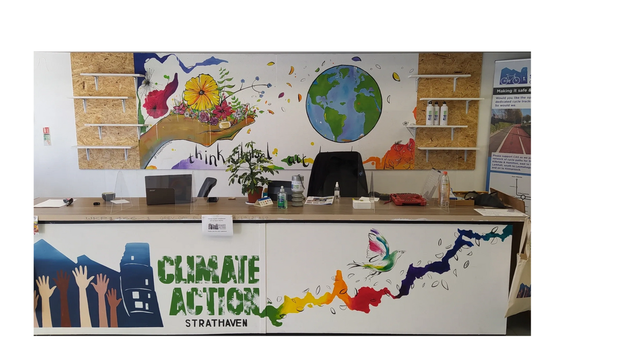 The Climate Action Strathaven desk in the Eco Hub, with colourful hand painted mural behind