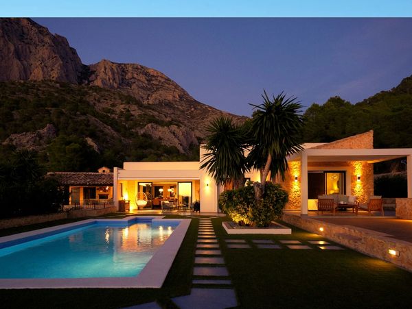 Modern villa with illuminated pool at dusk against mountain backdrop.