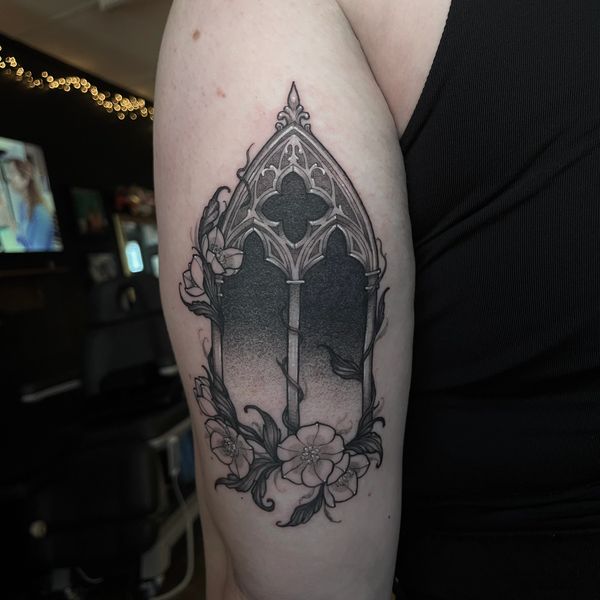 Black and grey tattoo of a gothic window with flowers on the arm.