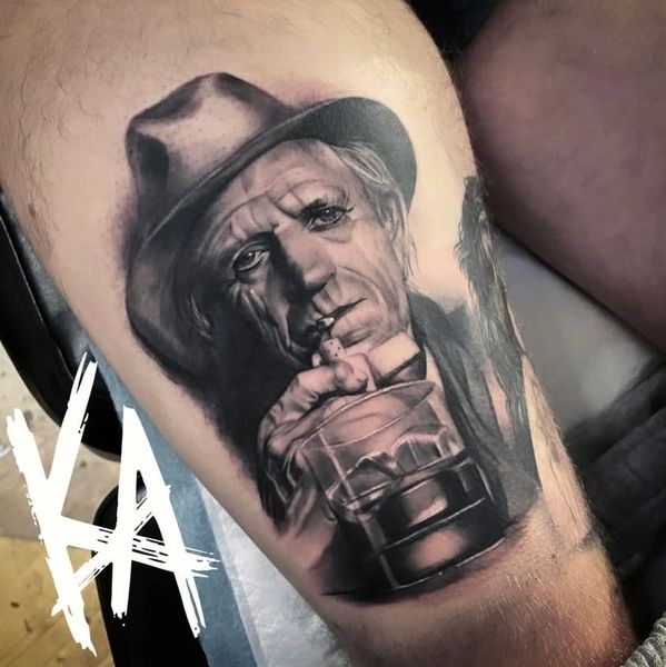 Realistic black and grey portrait tattoo of Keith Richards with a hat, holding a cigarette and a glass of whiskey.