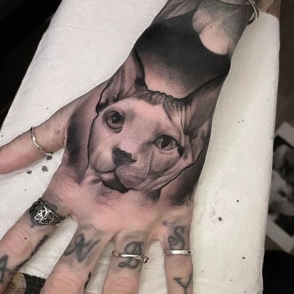 Black and gray tattoo of a cat's face on the back of a hand.