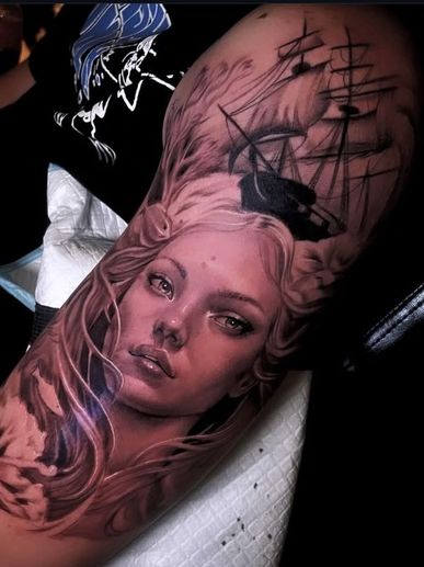 Realistic tattoo of a woman's face with flowing hair and a sailing ship above her head.
