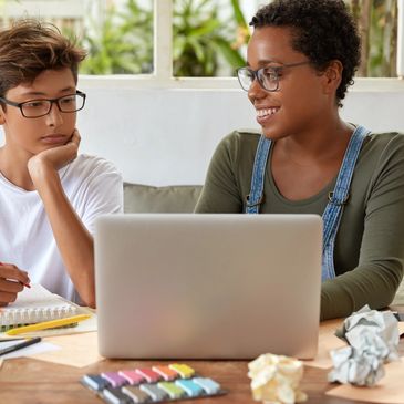 A woman helps a boy with homework using a laptop.