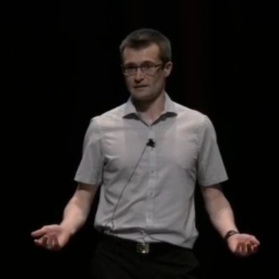 Man in glasses speaking on stage with a microphone.