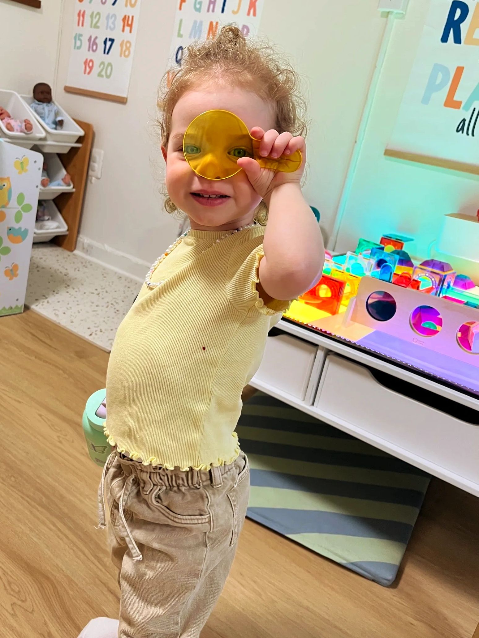Child playing with a yellow transparent toy in a colorful playroom.