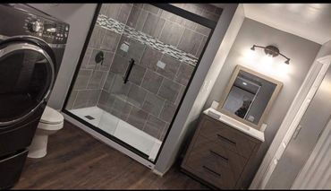 Stylish laundry room, a front-loading washer & dryer. a walk-in tiled shower, & vanity with a mirror.