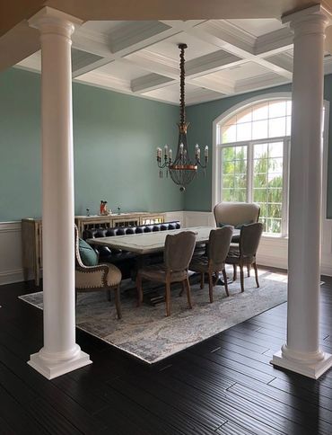 Elegant diningroom with tall white columns, wood flooring, a coffered ceiling, a large arched window