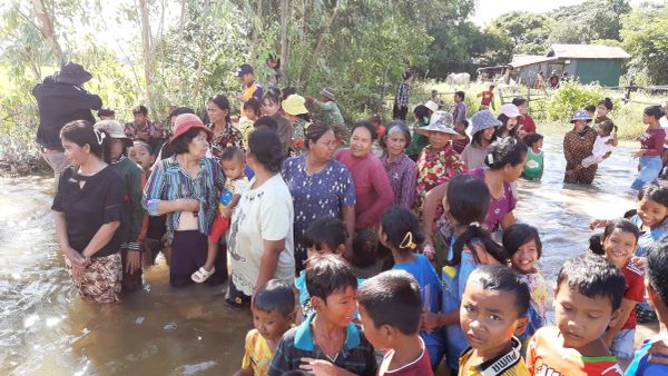 A large group of people, mostly children and women, standing in shallow water outdoors.