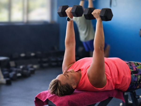 Woman lifting dumbbells on a bench in the gym.