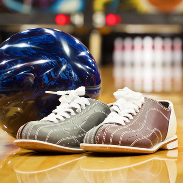Bowling ball and shoes resting on a lane with a full set of pins lined up 