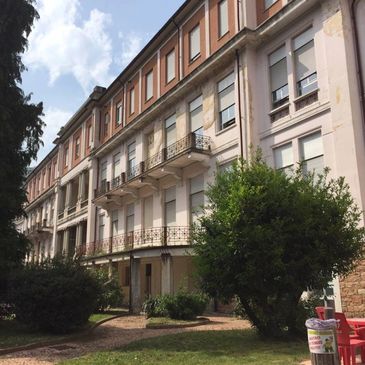 Historic multi-story building with balconies and greenery in front.