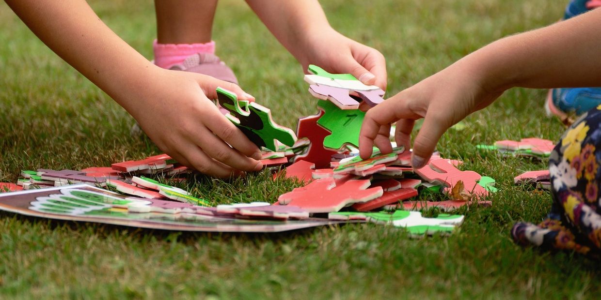 Children assembling a colorful puzzle on the grass outdoors.
