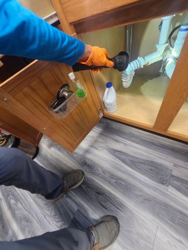 Person inspecting pipes under a sink with a flashlight.