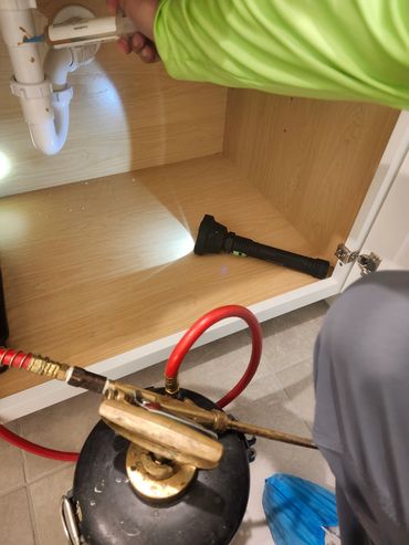 Person fixing plumbing under a sink with tools and flashlight.