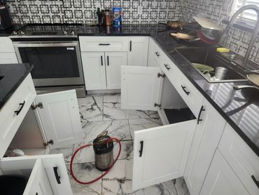 Kitchen cabinets open with a spray tank on the floor.