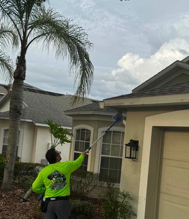 Pest control worker inspecting roof with tool outside a house.