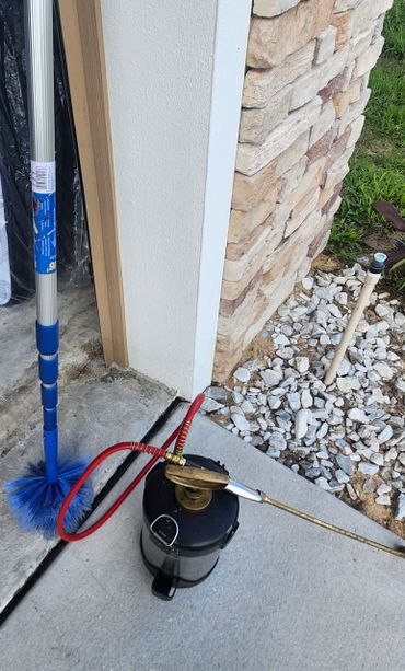 Outdoor cleaning tools including a blue brush and a sprayer near a stone wall.