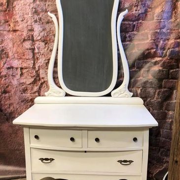 White vintage dresser with mirror against a brick wall.