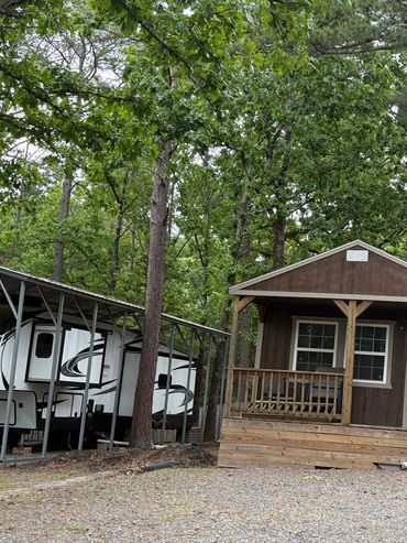 Small cabin surrounded by trees and an RV carport.