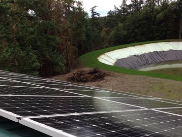 Solar panels installed on a green metal roof with trees and a small pond in the background.