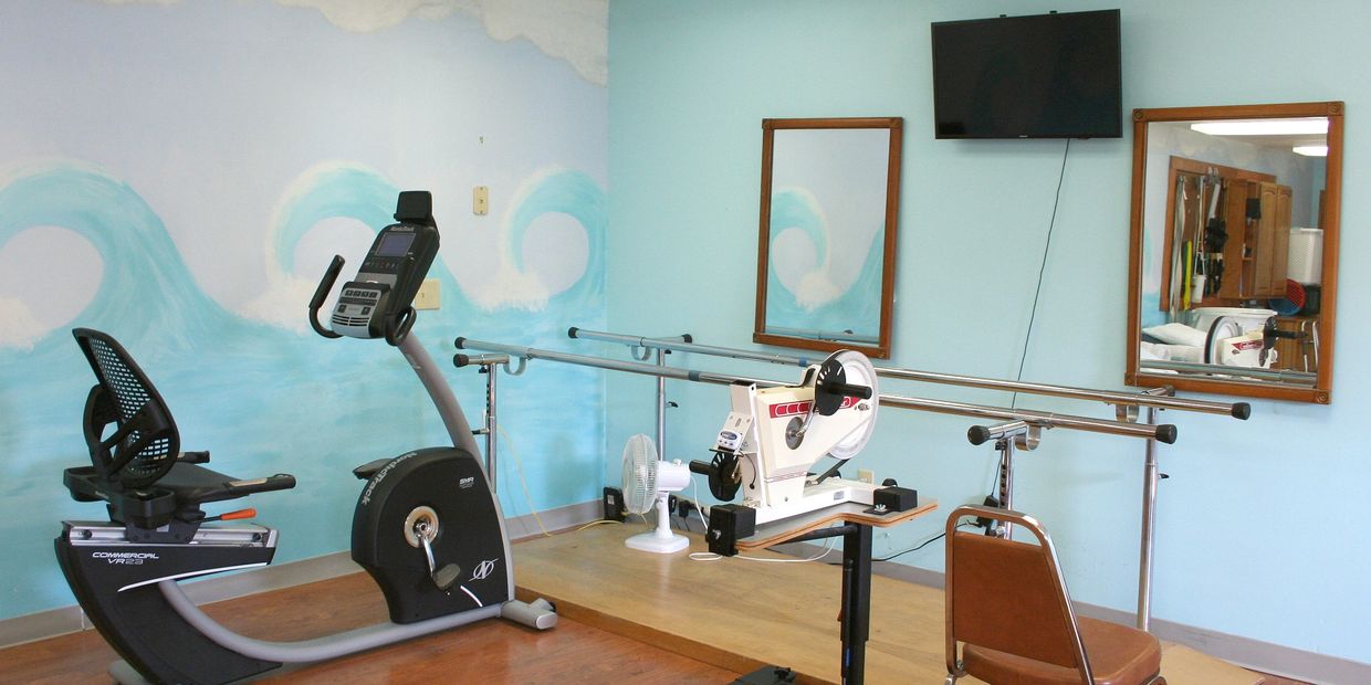 Physical Therapy Room with recumbent bike, hand therapy, and parallel bars.