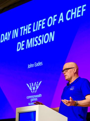 Man giving a presentation titled 'Day in the Life of a Chef De Mission'.