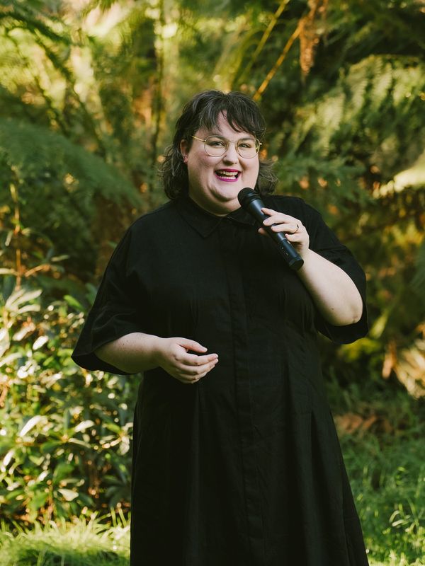Person in black dress speaking with a microphone outdoors.