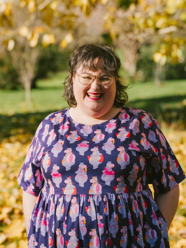 Woman smiling outdoors in a purple dress with hippo prints.