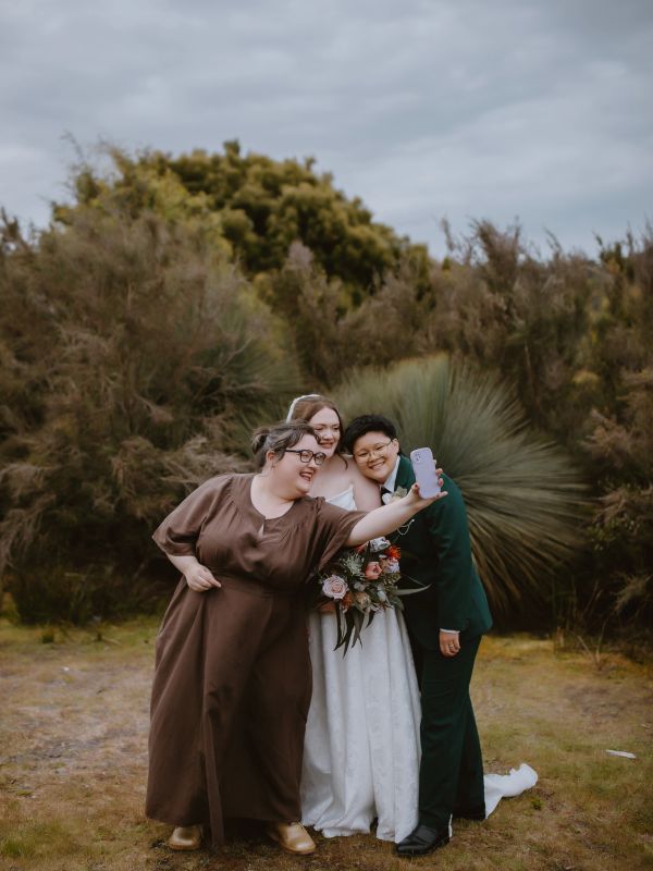 Three friends taking a selfie outdoors, celebrating a wedding.