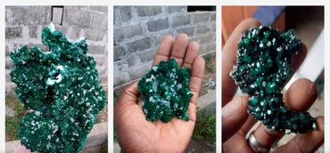 Close-up of vibrant green crystals held in hands against a rough stone wall.