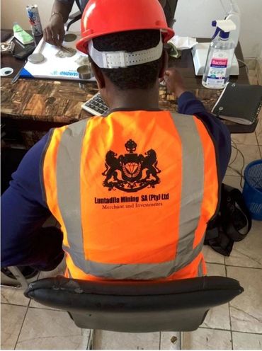 Person in high-visibility mining vest and helmet at a desk with mining samples.