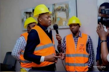 Men wearing yellow hard hats and orange safety vests during an interview.