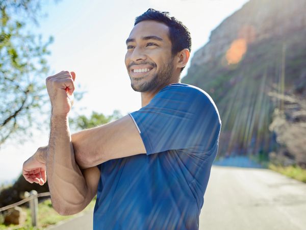 Smiling man stretching outdoors on a sunny day.