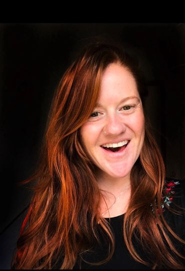 Smiling woman with long red hair and a nose ring.