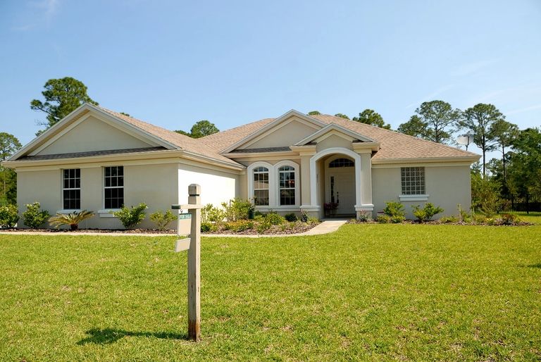 White and brown concrete bungalow under clear blue sky, for sale, to be inspected.