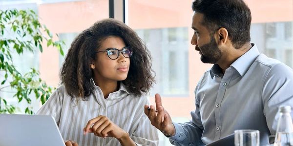 Two coworkers discussing at an office desk.
