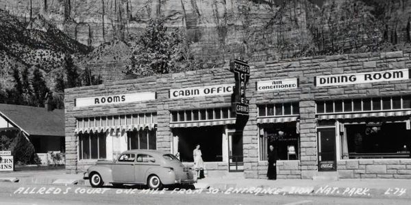 Vintage roadside cabins and dining room with classic car parked outside.