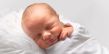 Newborn baby peacefully sleeping wrapped in a white blanket.