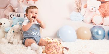 A baby celebrates a first birthday with cake and balloons.